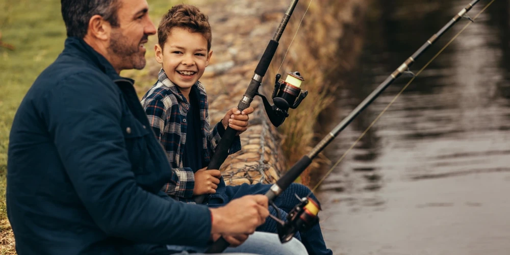 A smiling man and his son fishing at a lake