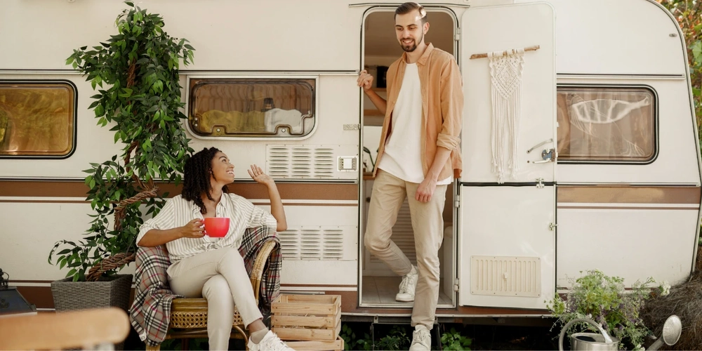 Man on steps of RV while woman relaxes on a seat in front of the RV