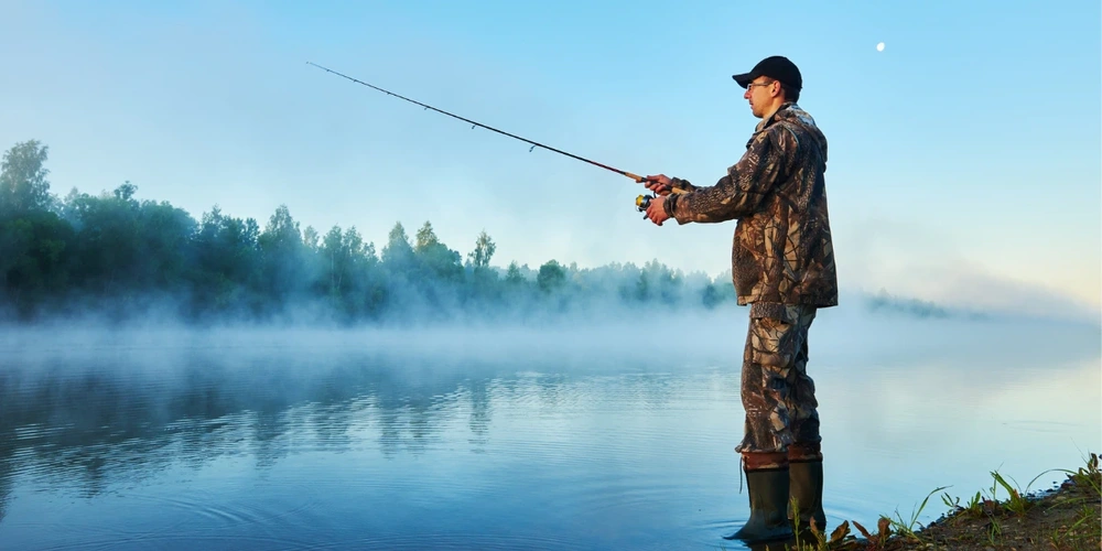 Man standing on lake edge and fishing during a foggy morning