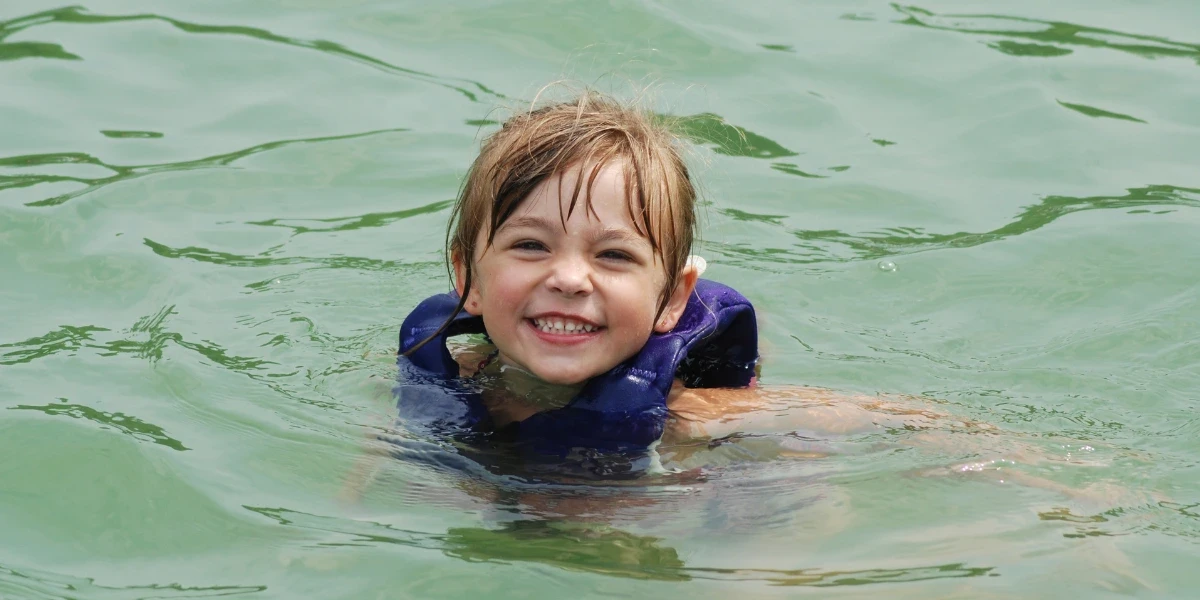 A little girl wearing a life jacket, floating and swimming in the lake