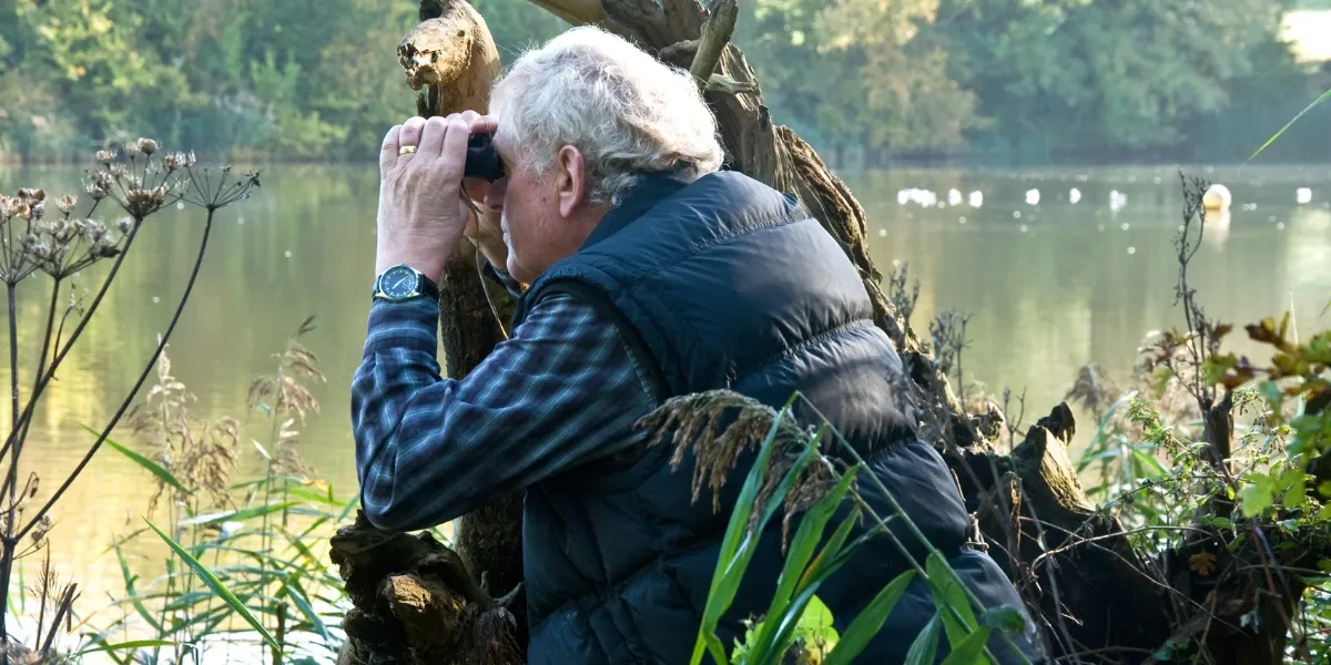 Old man with binoculars bird watching by the lake