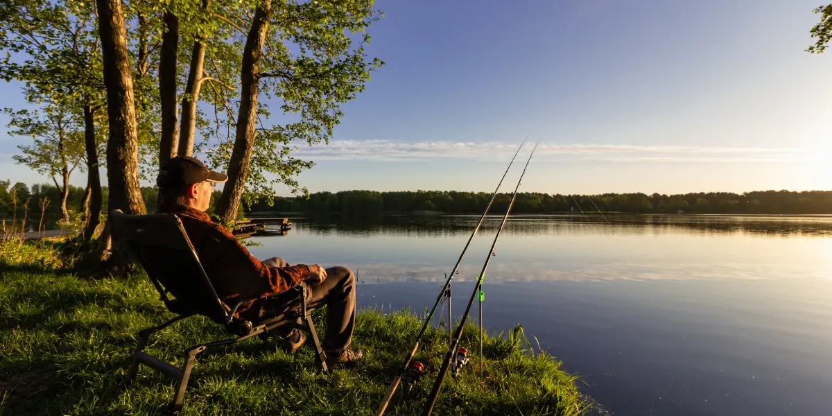 An angler sitting on the shore of the lake during sunrise