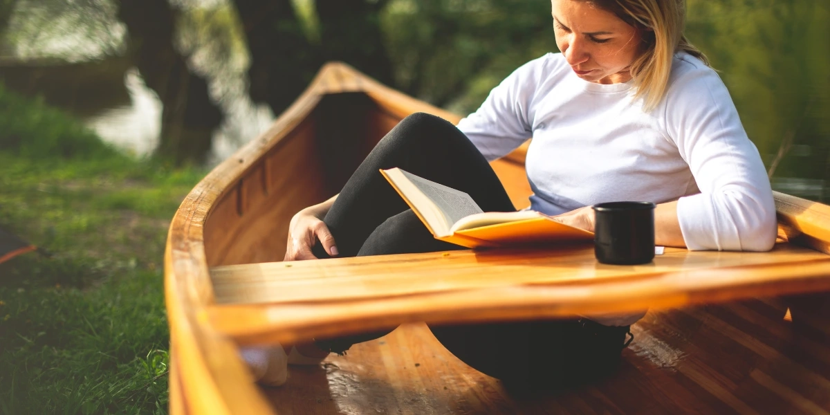 Woman sitting on a canoe on the ground and reading