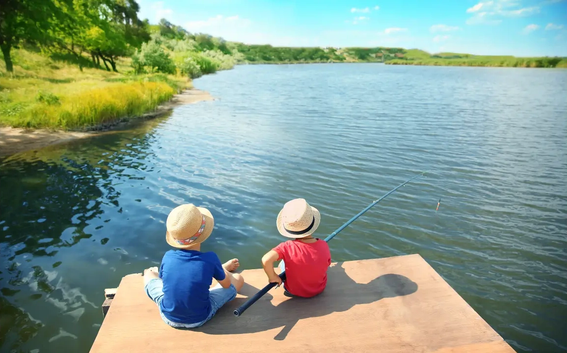 2 kids fishing along a lake's shoreline.