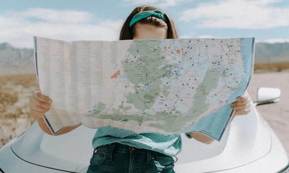 A woman in front of her car looking at a map for directions