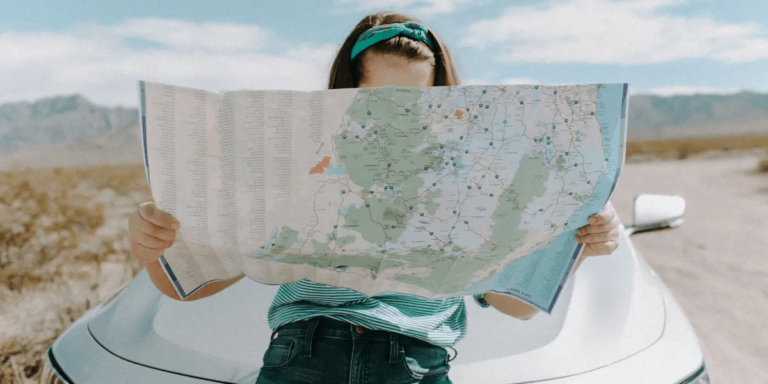 A woman in front of her car looking at a map for directions